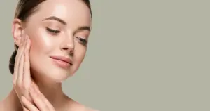 Young woman with glowing, flawless skin gently touching her cheek with both hands, eyes closed, after receiving Sofwave treatments in Valencia, CA.